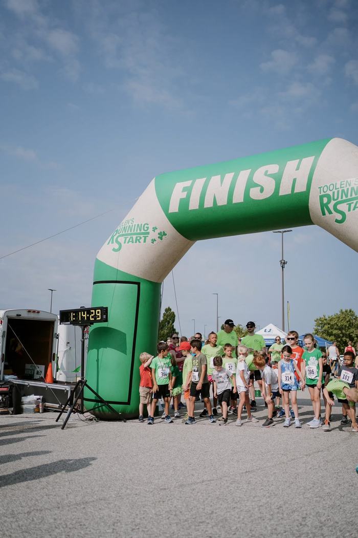Kids lining up near the green Toolens Running Start finish arch