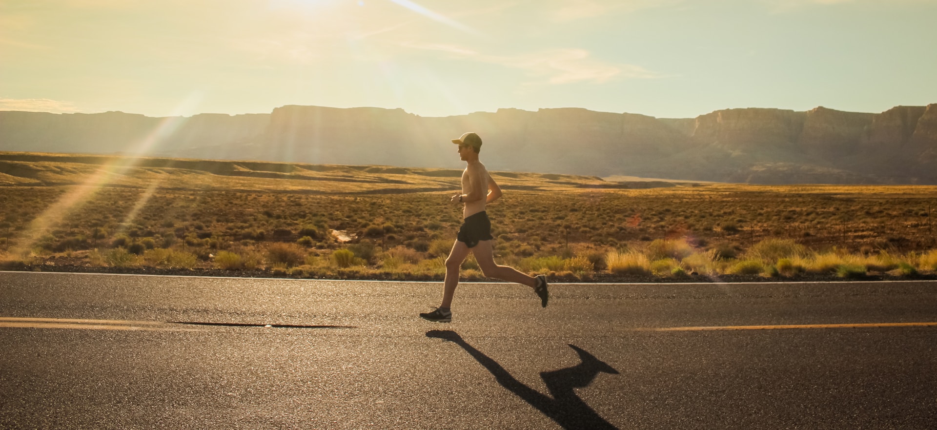Runner wearing a cap and shorts running on a sun-drenched desert road