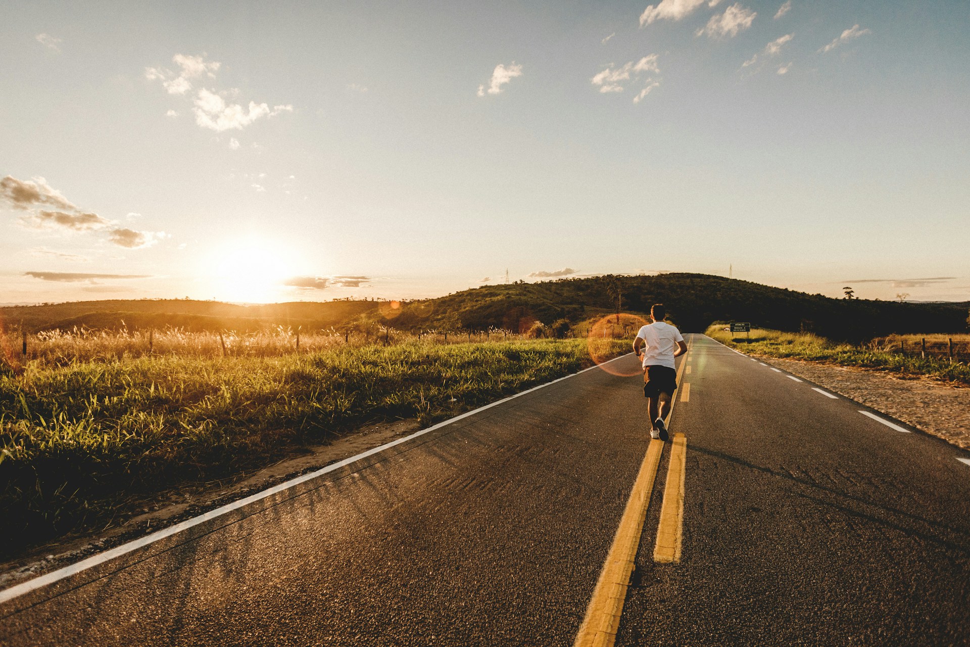 Runner in a light-colored shirt running down a country road at sunset